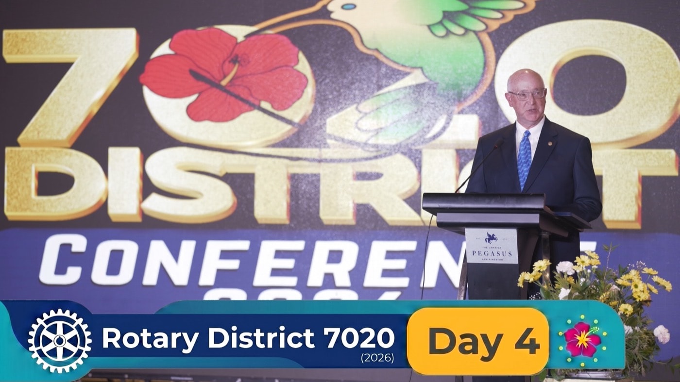 A speaker addresses delegates from the lectern beneath the District 7020 Conference backdrop at the Jamaica Pegasus.